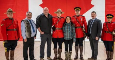 Inuuki Burke entouré de ses parents, amis et représentants du Nunavut devant le drapeau canadien.