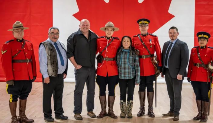 Inuuki Burke entouré de ses parents, amis et représentants du Nunavut devant le drapeau canadien.