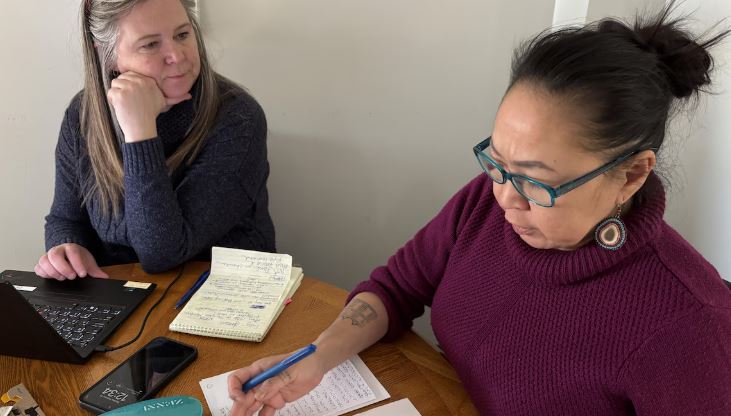 Deux femmes assises à une table avec des notes papier discutent le 26 février 2025.