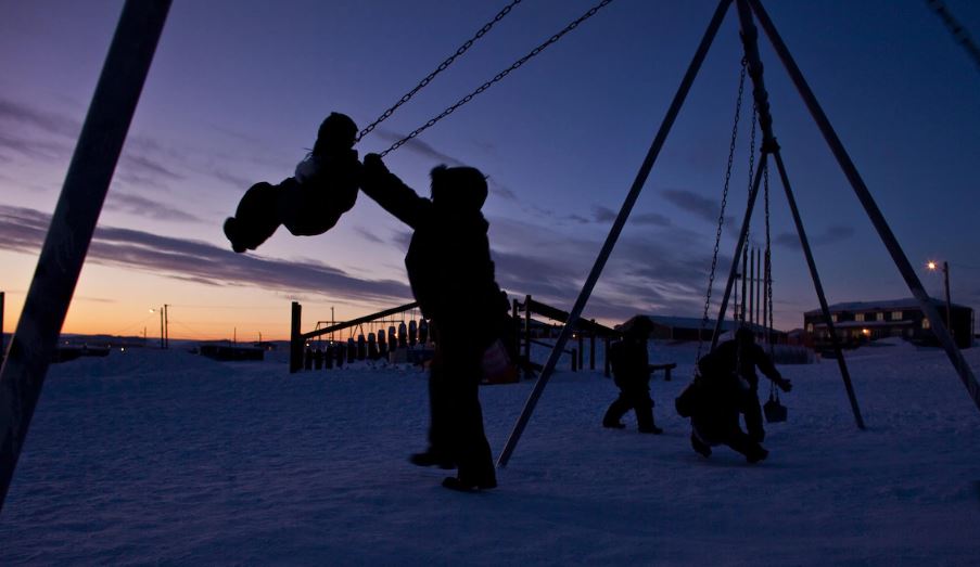 Des enfants jouent sur une balançoire à Iqaluit, au crépuscule.