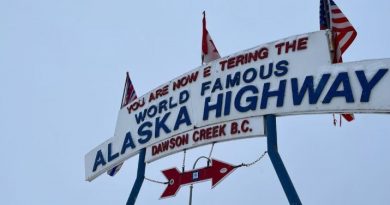 Une enseigne d'accueil vers la route de l'Alaska, où trois drapeaux sont accrochés: les drapeaux de la Colombie-Britannique, du Canada et des États-Unis.