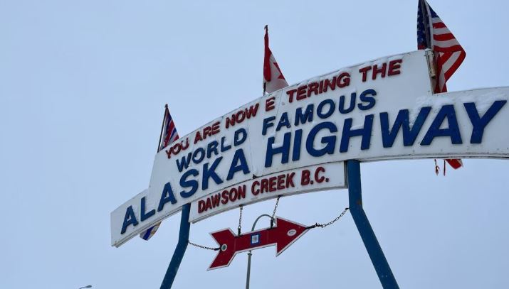 Une enseigne d'accueil vers la route de l'Alaska, où trois drapeaux sont accrochés: les drapeaux de la Colombie-Britannique, du Canada et des États-Unis.