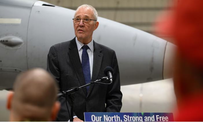 Bill Blair derrière un micro et devant un avion militaire, le 6 mars 2025.