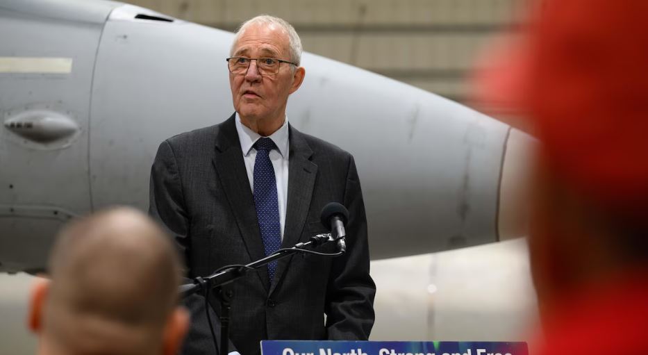 Bill Blair derrière un micro et devant un avion militaire, le 6 mars 2025.