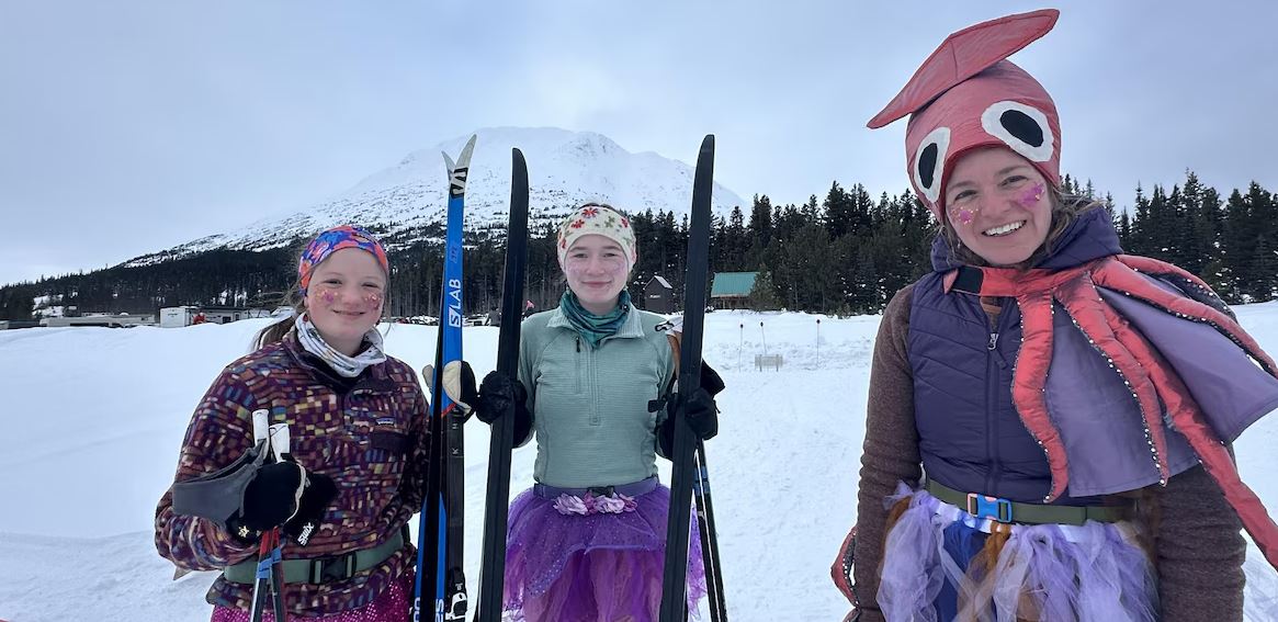 De jeunes participantes déguisées sourient pour la pose avec des skis entre les bras, le 15 mars 2025.