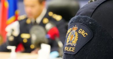 Gros plan sur le blason de la GRC cousu sur un chandail d'un membre de la force. Au deuxième plan, flou, un agent de police s'exprime aux micros.