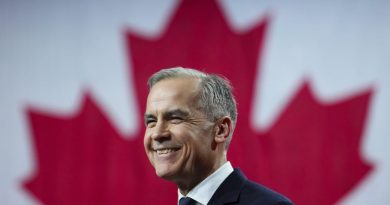 Mark Carney sourit sur une scène devant un immense drapeau canadien.