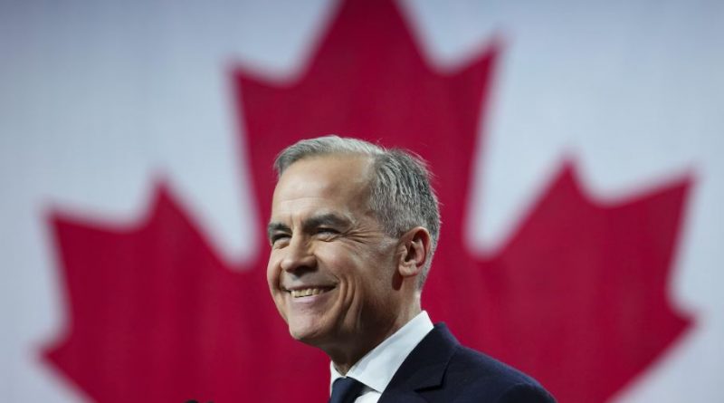 Mark Carney sourit sur une scène devant un immense drapeau canadien.
