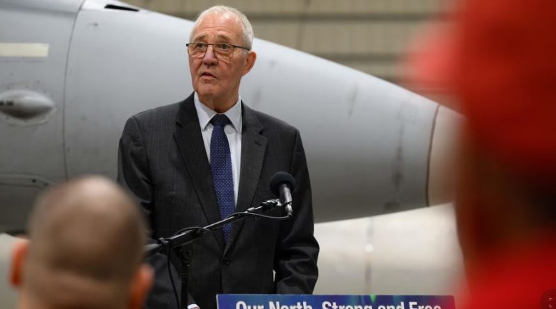 Bill Blair derrière un micro et devant un avion militaire, le 6 mars 2025.