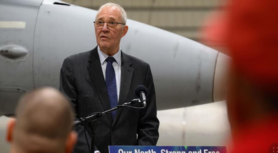 Bill Blair derrière un micro et devant un avion militaire, le 6 mars 2025.