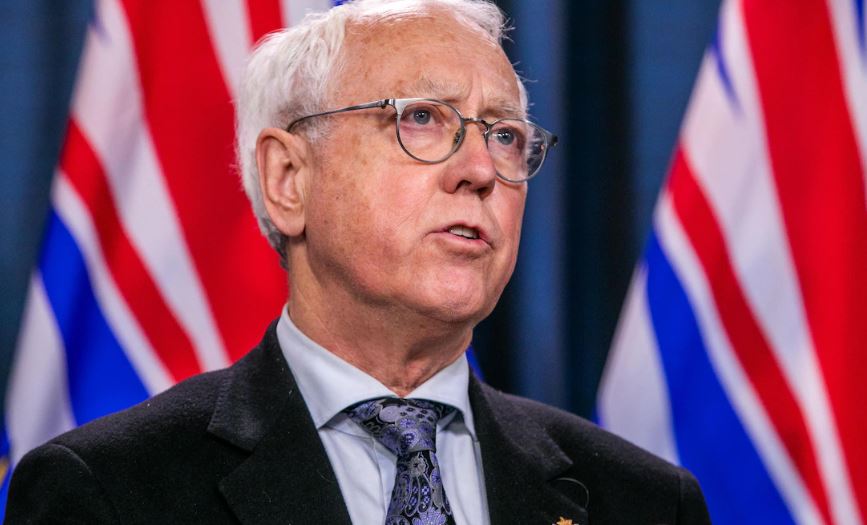 Portrait du ministre des relations avec les Autochtones et de la réconciliation, Murray Rankin, devant des drapeaux.