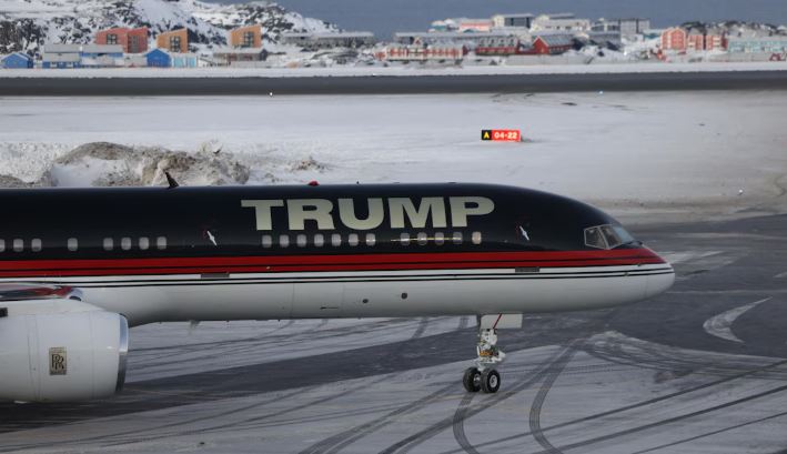 Un avion sur lequel est écrit « Trump » est posé devant un paysage de neige et de maisons.