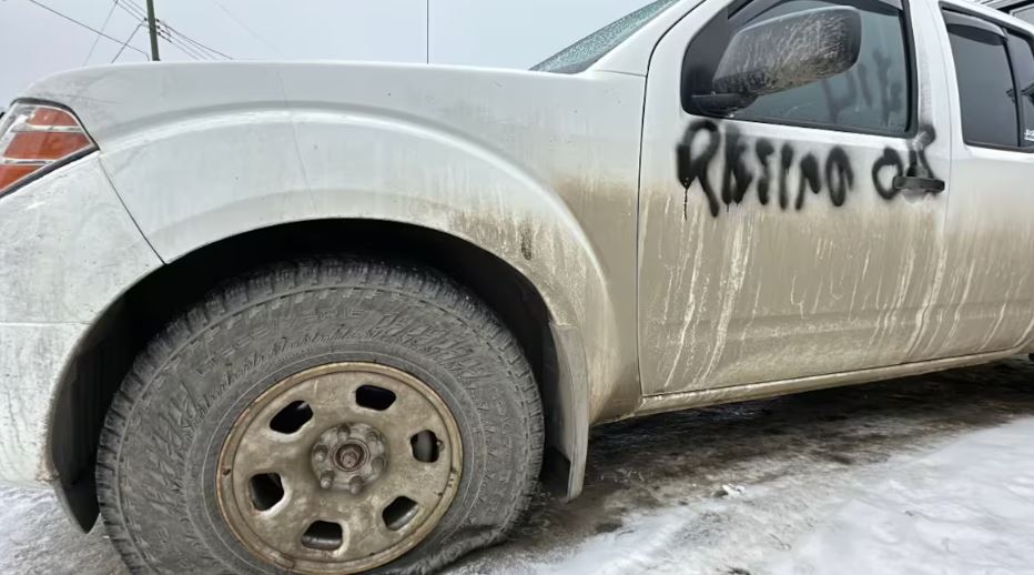 Le côté avant gauche de la voiture avec le pneu crevé et le message «démissionne ou meurt» sur la portière.