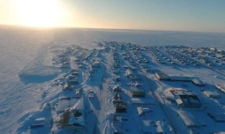 La communauté d'Arviat sous la neige photographiée de haut en avril par un drone avec le soleil à l'horizon.