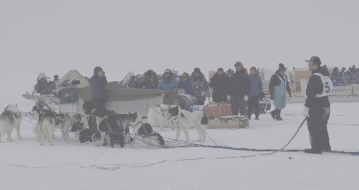 Un attelage de chiens et un groupe de résidents attendent sur la banquise près de Pond Inlet, avant le départ de la Nunavut Quest, le 15 avril 2025.
