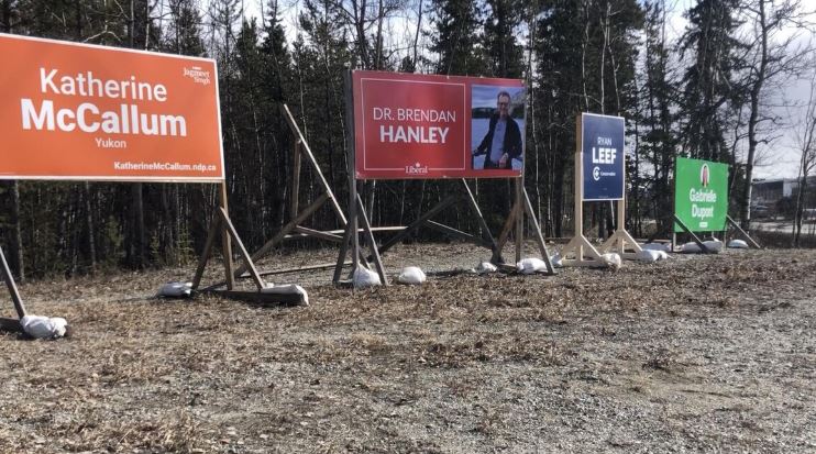 Quatre grandes pancartes sur le bord d'une rue au soleil, le 12 avril.