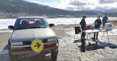 Un bureau de vote installé en extérieur au bord du fleuve Yukon à côté d'une camionnette et trois personnes.