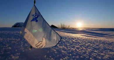 Un petit drapeau bleu et blanc arborant les symboles d'un ours polaire et d'un logo représentant une moitié de fleur de lys et une moitié de flocon est planté dans la neige.