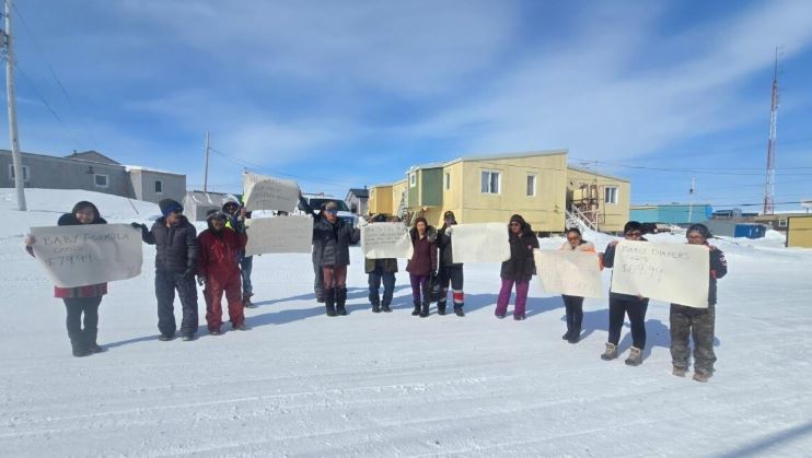 Une douzaine de personnes manifestent dans une rue enneigée d'Igloolik, au Nunavut, le 24 avril 2025, en tenant des pancartes à la main.