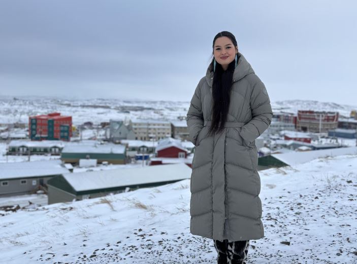 Une femme vêtue d'un long manteau d'hiver se tient debout devant une vue enneigée d'Iqaluit, au Nunavut, en décembre 2024.