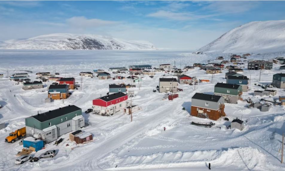 Le village enneigé avec plusieurs maisons bicolores est réparti de part et d'autre d'une petite route.
