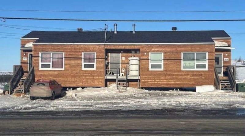 Une maison de bois avec une cuve de mazout encastrée au centre sur un paysage enneigé.