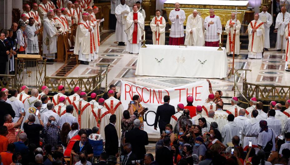 Deux manifestants autochtones tiennent une banderole devant l'autel de la basilique de Sainte-Anne-de-Beaupré.