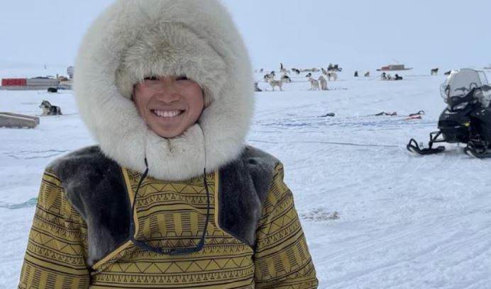 Une femme vêtue d'un manteau traditionnel se tient debout devant des chiens de traîneau, durant le début de la course Nunavut Quest, à Pond Inlet, au Nunavut, le 15 avril 2025.