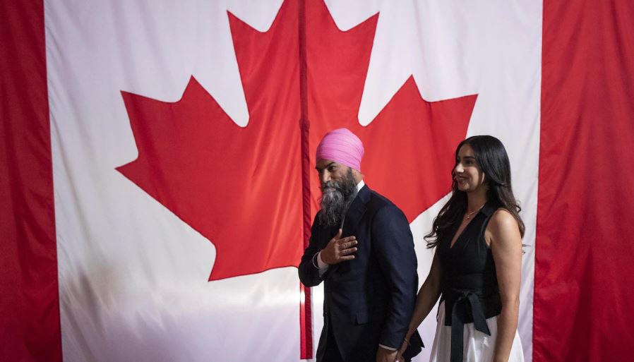 Jagmeet Singh et sa femme devant un grand drapeau canadien.