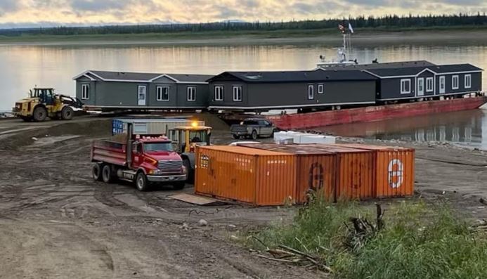 Trois maisons modulaires sont retirées d'une barge le long d'un fleuve à Tulita.