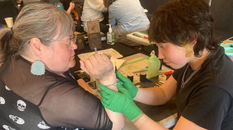 Une artiste autochtone applique un tatouage traditionnel à la main sur l’avant-bras d’une participante, lors d’un rassemblement culturel à Whitehorse.