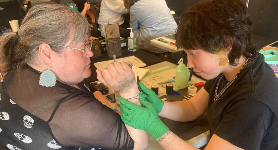 Une artiste autochtone applique un tatouage traditionnel à la main sur l’avant-bras d’une participante, lors d’un rassemblement culturel à Whitehorse.