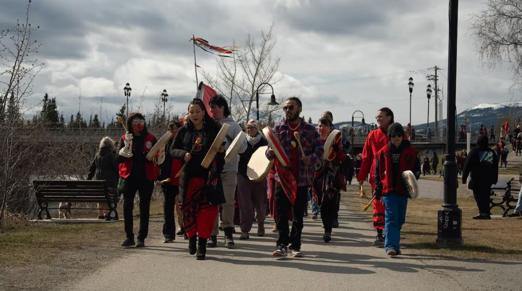 Des personnes jouent du tambour traditionnel en marchant le long du fleuve Yukon, à Whitehorse, le 5 mai 2025.