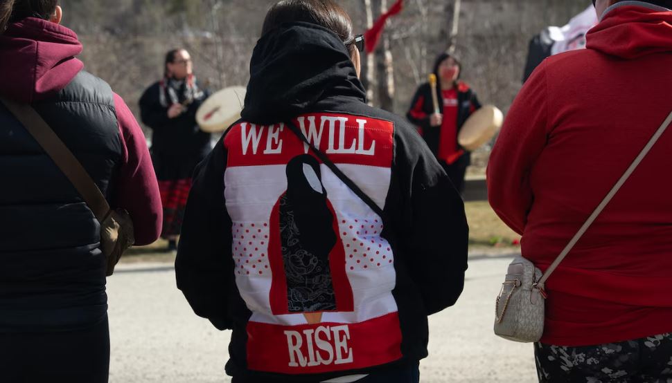 Des personnes rassemblées, dont une de dos avec un manteau sur lequel est écrit We will rise, le 5 mai, à Whitehorse.