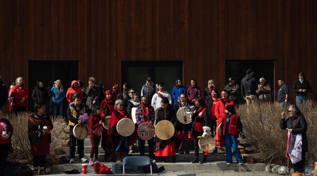 Des personnes habillées de rouge tiennent des tambours derrière le centre culturel Kwanlin Dün, le 5 mai 2025.