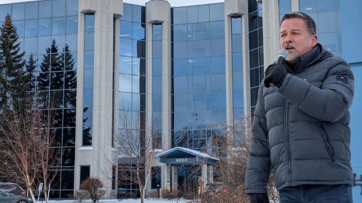 Larry Imbeault parle dans un micro devant un bâtiment.