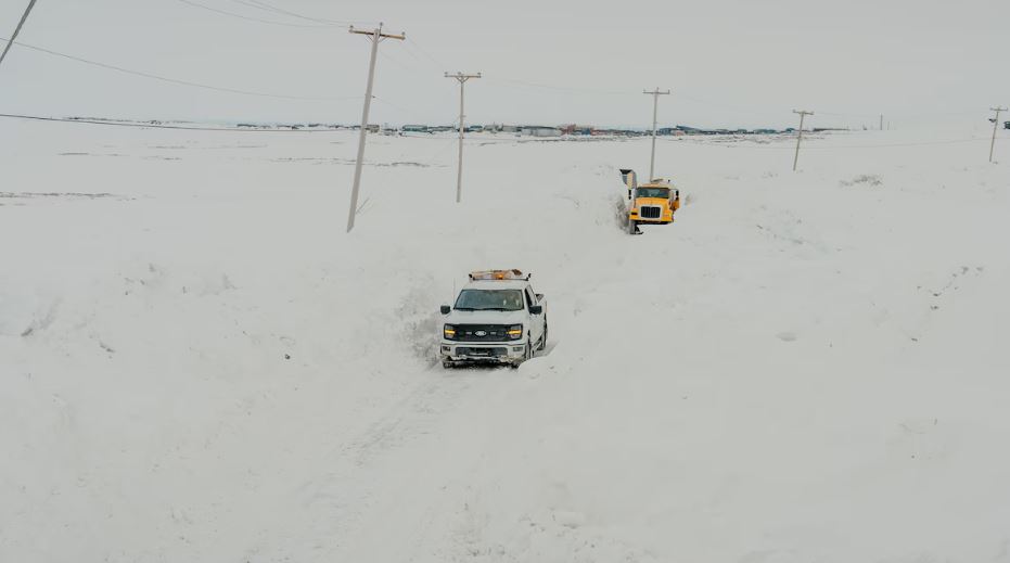 Deux camions sur une petite route bordée de neige à Puvirnituq, le 19 mai 2025.