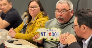 Un homme assis à côté de plusieurs personnes tient une plaque d'immatriculation en forme d'ours polaire, à Iqaluit, au Nunavut, le 20 mai 2025.