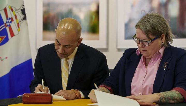 Ranj Pillai et Kate White signent un document devant un drapeau du Yukon.