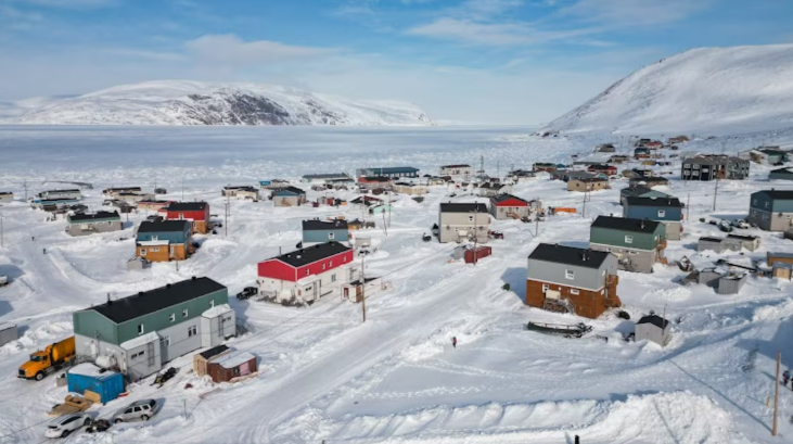Le village enneigé avec plusieurs maisons bicolores est réparti de part et d'autre d'une petite route.
