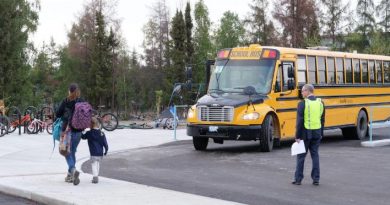 Une personne observe un parent avec son enfant marchant sur un trottoir, devant un autobus scolaire.