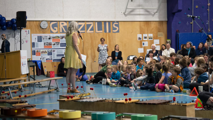 Une personne debout devant un public d'enfants et d'adultes dans le gymnase de l'École Emilie Tremblay, à Whitehorse, au Yukon.