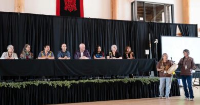 Huit personnes assises à une longue table et deux autres debout qui tiennent un tambour traditionnel.