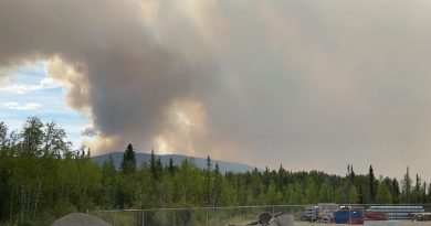 Une épaisse fumée s'élève au-dessus d'une montagne avec en avant-plan du matériel de construction gardé par une clôture.