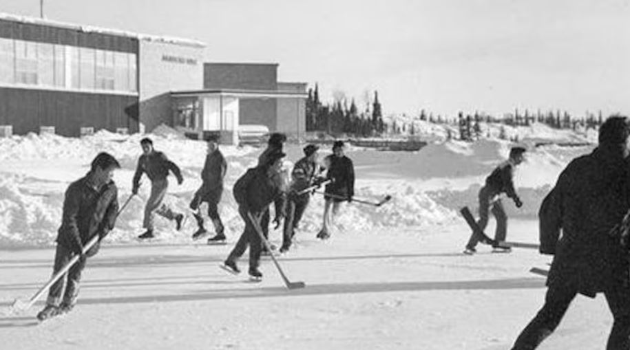 Une image en noir et blanc de personnes sur un patinoire devant Akaitcho Hall. 