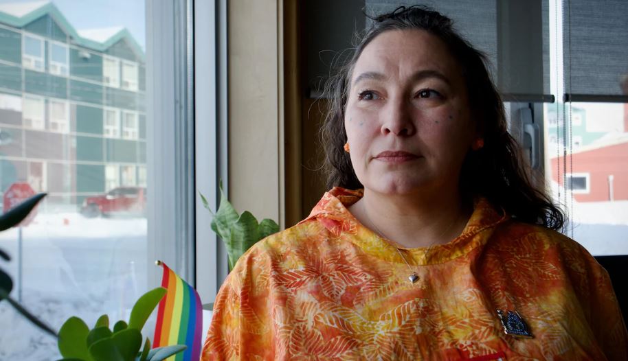 Une femme vêtue d'un haut orange regarde à travers la fenêtre de son bureau, à Iqaluit, au Nunavut, le 7 mars 2024.