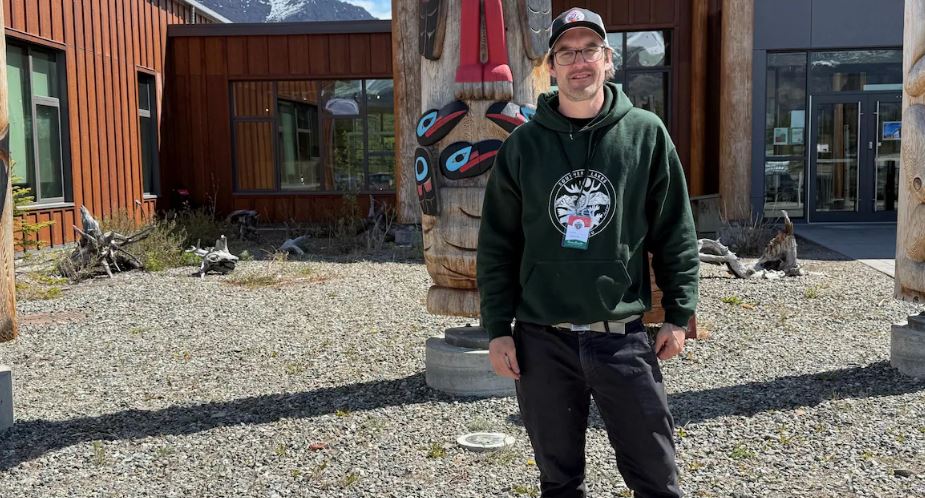Lars Jessup debout devant des totems regarde vers l'appareil photo.