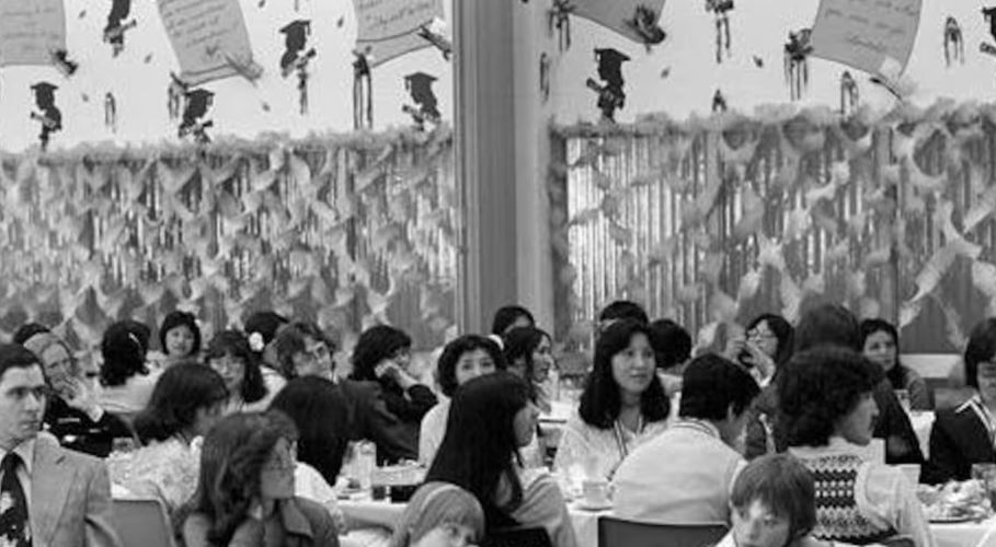 Une photo et noir et blanc de personnes assises à des tables dans une salle décorée.
