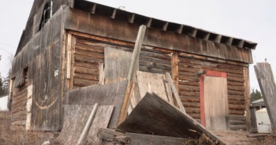 Une maison en bois avec des plaque de bois entreposées autour.