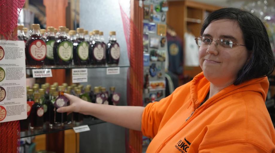Une femme travaille à l'ordinateur de la caisse d'un magasin de siouvenirs. Elle porte une veste orange.